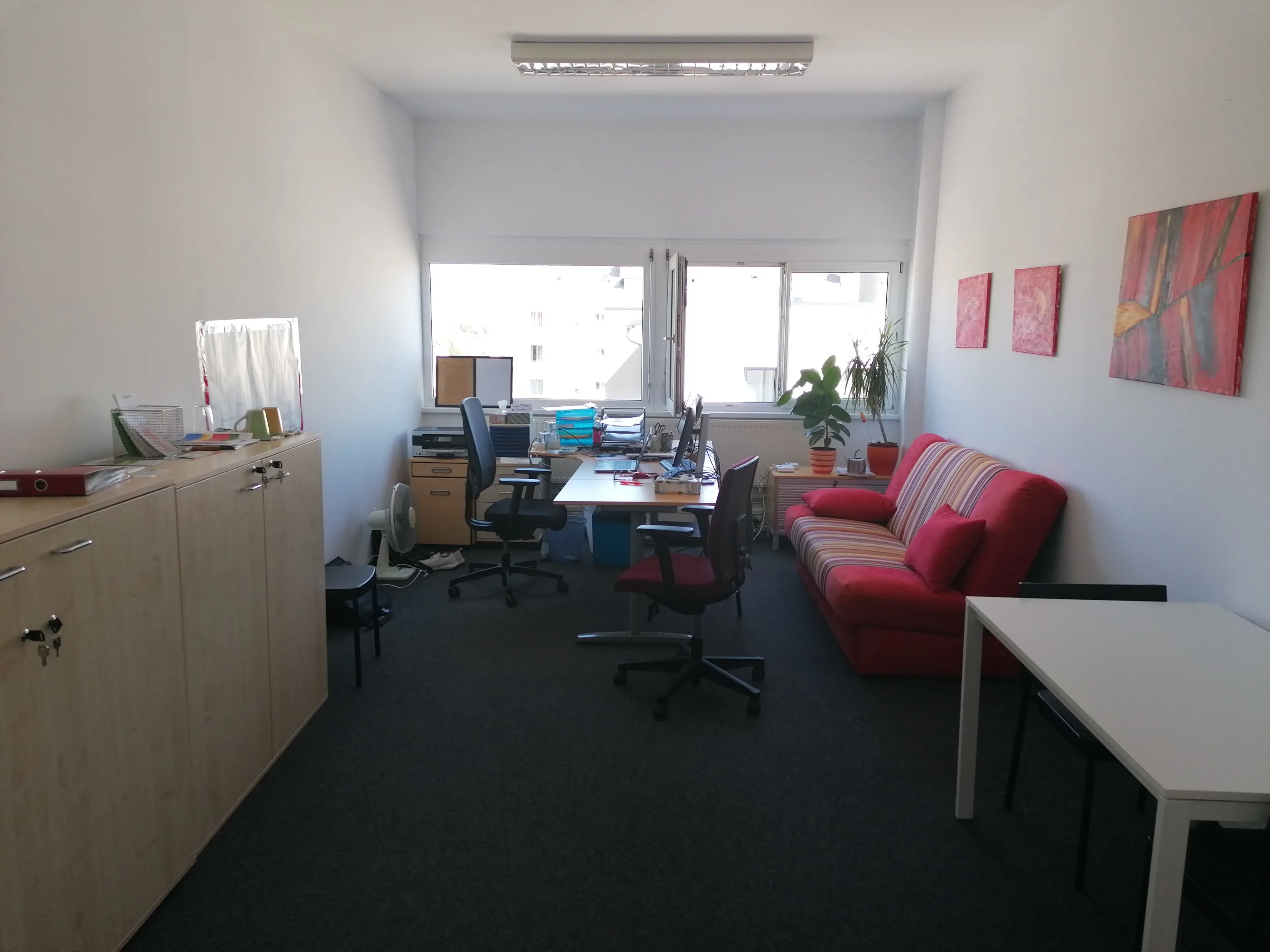 Büro vor der Umgestaltung mit roter Couch, Schreibtischen und unklaren Laufwegen